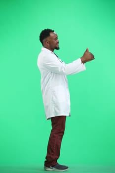 The doctor, in full height, on a green background, shows his thumbs up.