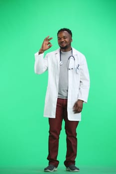 The doctor, in full height, on a green background, shows the ok sign.