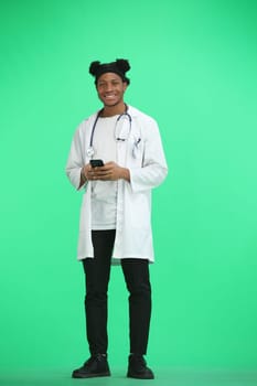 The doctor, in full height, on a green background, uses a phone.