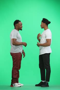 Men, in full height, on a green background, talking.