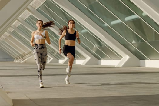 Two athletic women in sportswear is jogging around the city in early morning. Reaching the goal