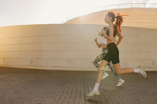 Two young women in sportswear are running on modern buildings background. Active lifestyle concept