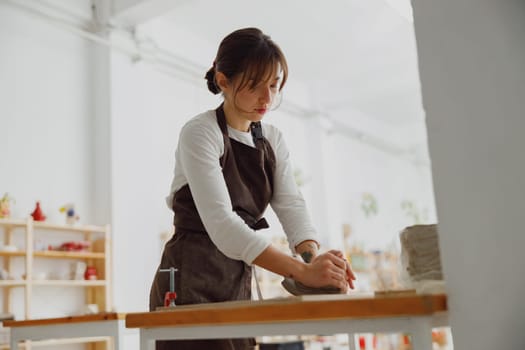 Pretty woman preparing clay to create a mug on a wooden table in pottery studio