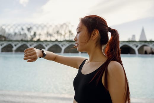 Young woman in sportswear looking on smartwatch before exercising. Outdoor sports in the morning