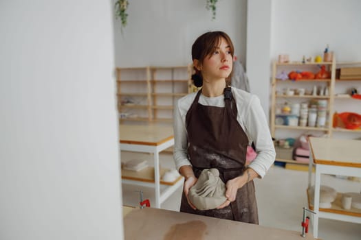 Pretty woman preparing clay to create a mug on a wooden table in pottery studio