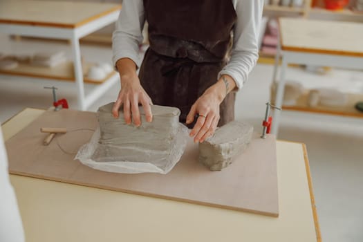 Close up of woman preparing clay to create a mug on a wooden table in pottery studio