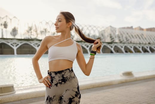 Pretty woman in sportswear have a rest after workout outside standing on building background