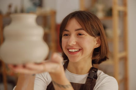 Young female potter holding unfired clay vase while standing in pottery studio. High quality photo