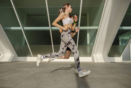 Two athletic women in sportswear is jogging around the city in early morning. Reaching the goal