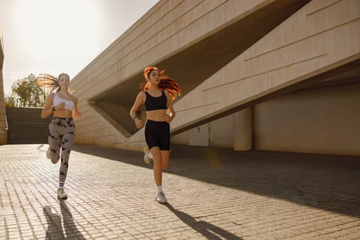 Two young women in sportswear are running on modern building background. Active lifestyle concept