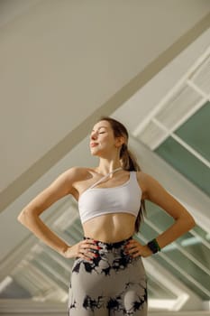 Young woman in sportswear have a rest after workout outside standing on building background