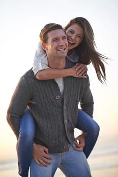 Portrait, piggy back and happy couple on beach at sunset for tropical holiday adventure, relax and bonding together. Love, man and woman on romantic date with ocean, evening sky and travel vacation