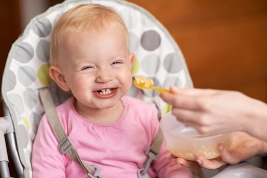 Happy, baby and laughing from feeding in high chair at home in the morning ready for eating food. Youth, funny and smile of a infant with development and laughter in house with fun and joy of a child.