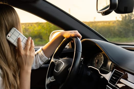 Young woman using mobile phone while driving car on highway road during sunset. Womandriver has accident calling with smartphone for help. Business woman busy driving concept