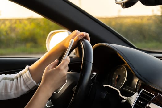 Woman sending messages with smartphone while driving automobile. Female driver using mobile phone on the road during driving the car. Safety and technology concept