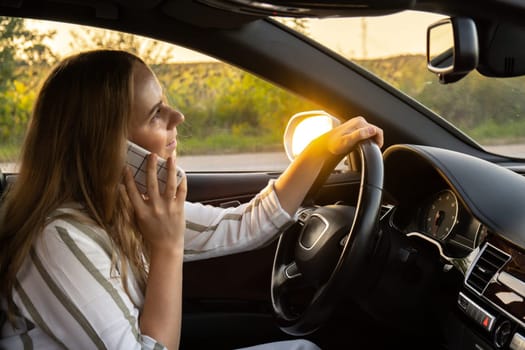 Happy young woman speaking by mobile phone while driving car. Business woman talking phone call in automobile. Unsafely risky driving. Concept of multitasking