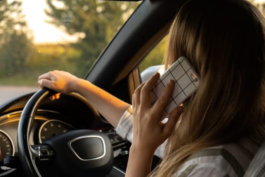 Happy young woman speaking by mobile phone while driving car. Business woman talking phone call in automobile. Unsafely risky driving. Concept of multitasking