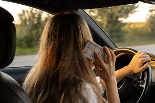 Young woman using mobile phone while driving car on highway road during sunset. Womandriver has accident calling with smartphone for help. Business woman busy driving concept