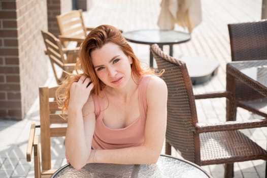 Beautiful young red-haired woman with braces on her teeth smiling while sitting in an outdoor cafe