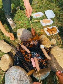 Campsite with friend. Cooking fried sausages and marshmallow on a fire in the forest.