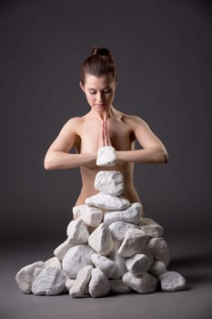 Meditating nude girl moves stones power of thought, on gray background