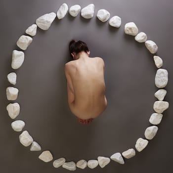 Bare woman posing lying in circle of stones. Top view