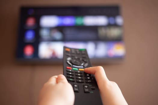 Children's hands hold a remote control on the background of a TV. High quality photo