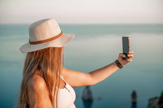 Selfie woman in hat, white tank top and shorts makes selfie shot mobile phone post photo social network outdoors on sea background beach people vacation lifestyle travel concept