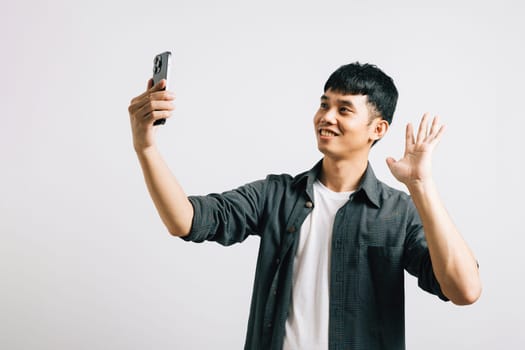 Portrait of a happy Asian man making a selfie on his smartphone in a studio setting, isolated on white background. A fun way to say hello to the camera.