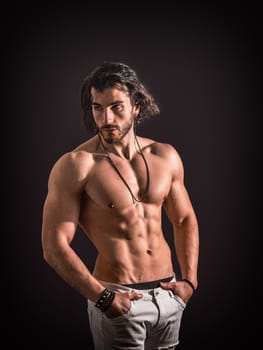 A man with long hair is standing shirtless, striking a pose for a photo. His toned physique is highlighted as he confidently gazes at the camera.