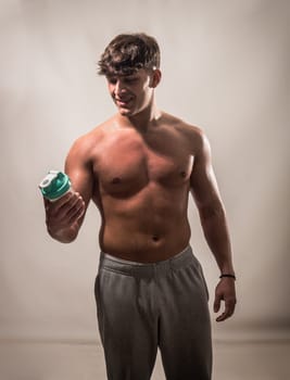 A man with no shirt is holding a green blender or shakerin his hand in this photo. He appears to be standing outdoors, with no other visible objects or people in the background.