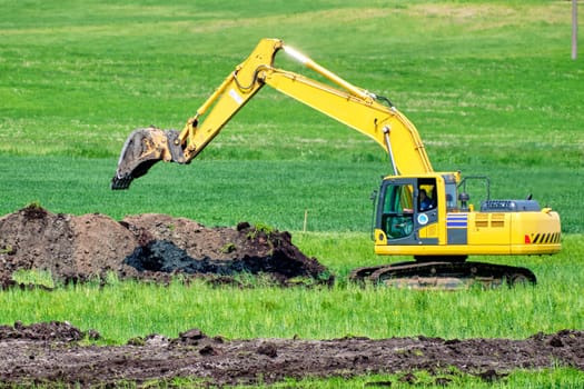 Yellow excavator while bathing the soil in an agricultural field