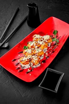 Delicious sushi rolls topped with golden brown seared cheese and seafood caps sprinkled with sesame and grated parmesan, garnished with greens served on red plate with soy sauce