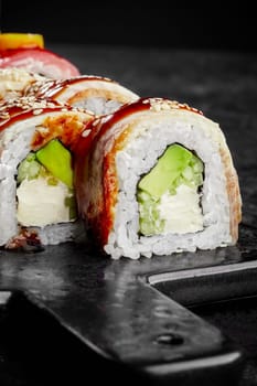 Closeup of appetizing fresh sushi rolls filled with cream cheese, avocado and cucumber topped with eel seasoned with unagi sauce sprinkled with sesame served on black board