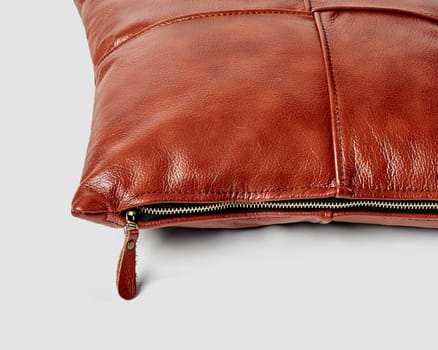 Handcrafted sofa pillow made from neatly stitched patches of smooth terracotta leather with convenient side zipper on white background, closeup view. Stylish artisan accessory for interior design