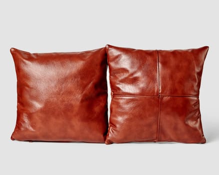 Pair of brown leather cushions showcasing smooth texture and expert stitching displayed side by side against white backdrop to emphasize warm tones and plush fullness. Crafted interior accessories