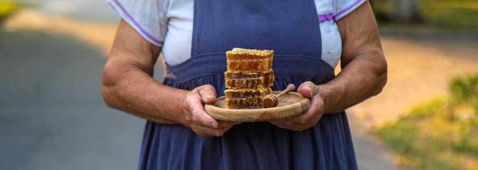 An elderly woman holds honey in her hands, selective focus. People.