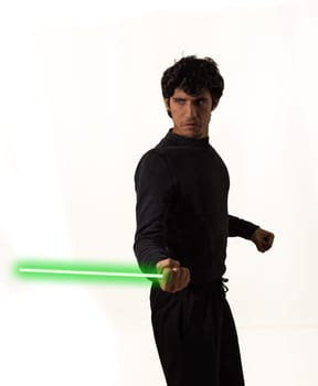 A man stands holding a green lightsaber in his right hand, ready for battle. The glowing weapon contrasts against the dark background, highlighting his determined expression.