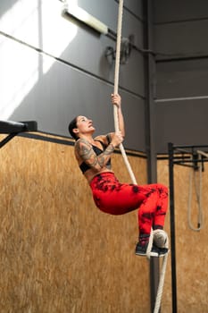 Vertical photo of a strong mature woman climbing a rope in a cross training gym