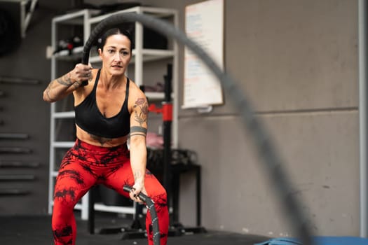 Female athlete training in a gym using battle rope sport equipment