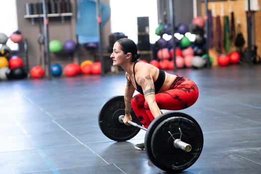 Side view of a mature sportive woman lifting weights in the gym