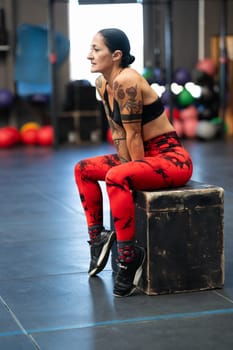 Vertical photo of a relaxed mature sportswoman sitting on a box in the gym