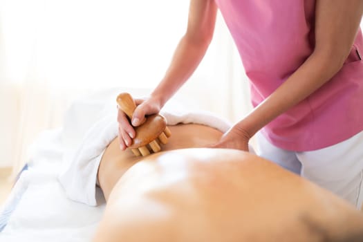 Crop professional therapist massaging with wooden therapy tool back of anonymous patient lying on table during rehabilitation session in physiotherapy clinic