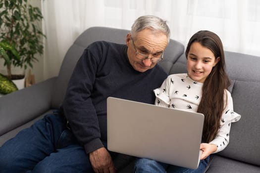 Happy retirement grandfather and pretty granddaughter laughing while watching e-book for learning to education together by laptop. Family educational at home concept. Technology and education