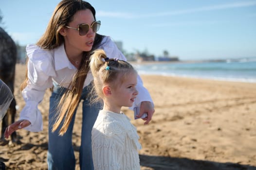 Young mother and daughter looking into the distance while walking together on the beach