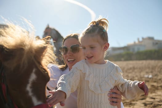 Authentic portrait of a young mother and her daughter smiling and stroking the pony