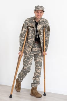 Portrait of soldier with crutches against white background.