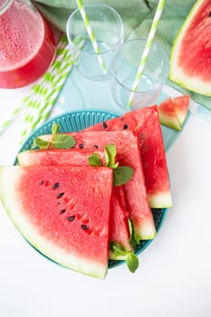 Fresh watermelon slices on a blue plate, garnished with mint, next to a refreshing smoothie and whole fruit