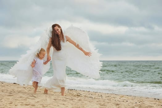 Sondervig, Denmark, August 22, 2023: Mom and daughter dressed as angels on the sea at sunset