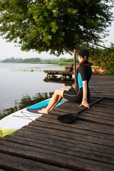 A girl in sportswear ready to paddleboard on a serene lake, surrounded by lush greenery
